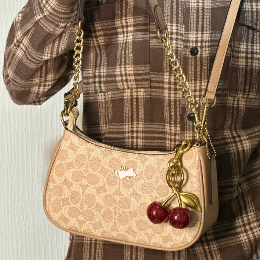 Beige handbag with cherry charm held by a person wearing a plaid shirt.