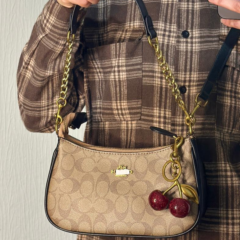 Person holding a beige handbag with a cherry charm against a neutral background