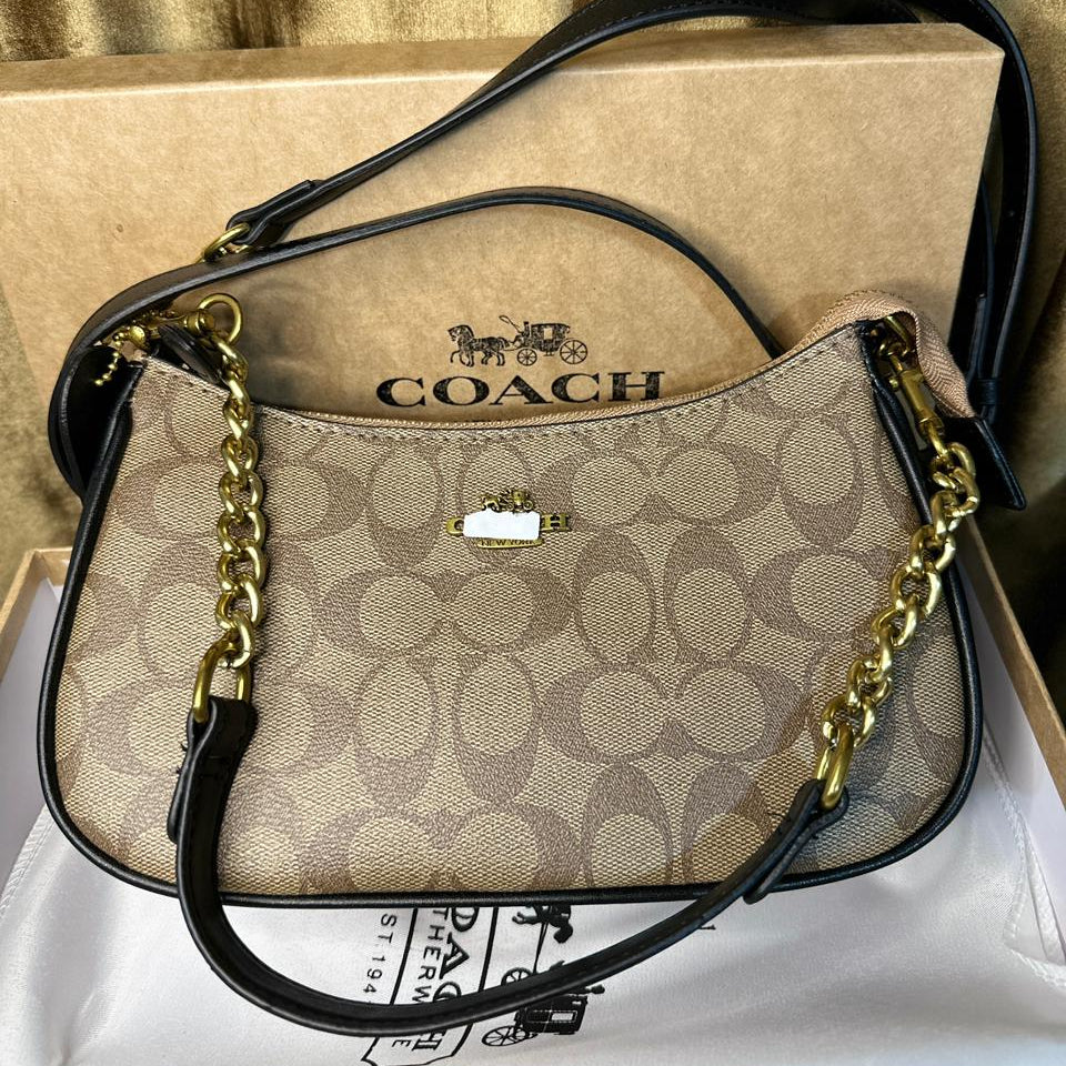 Coach handbag with gold chain strap on a white surface with Coach packaging in the background.